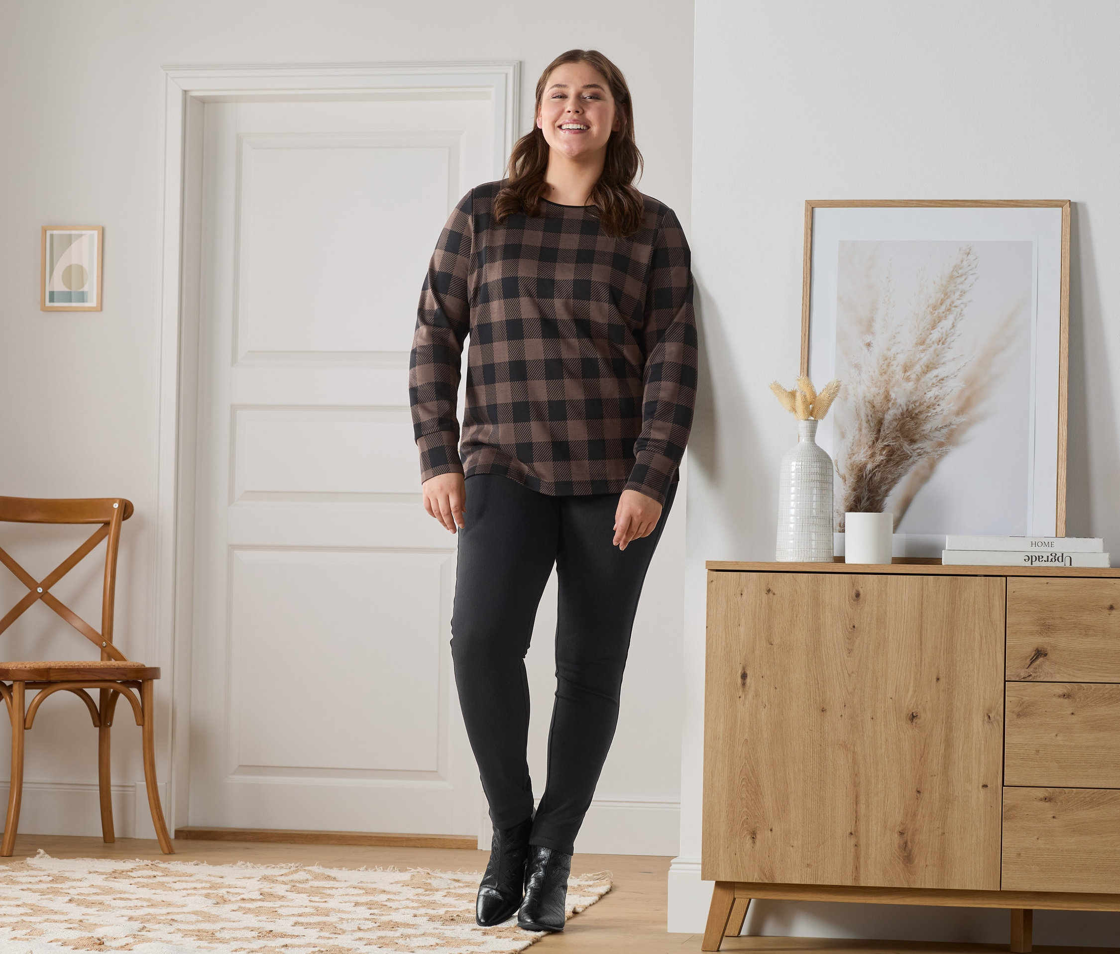 Kobieta pozuje w jegginsach i bluzie w kratę.