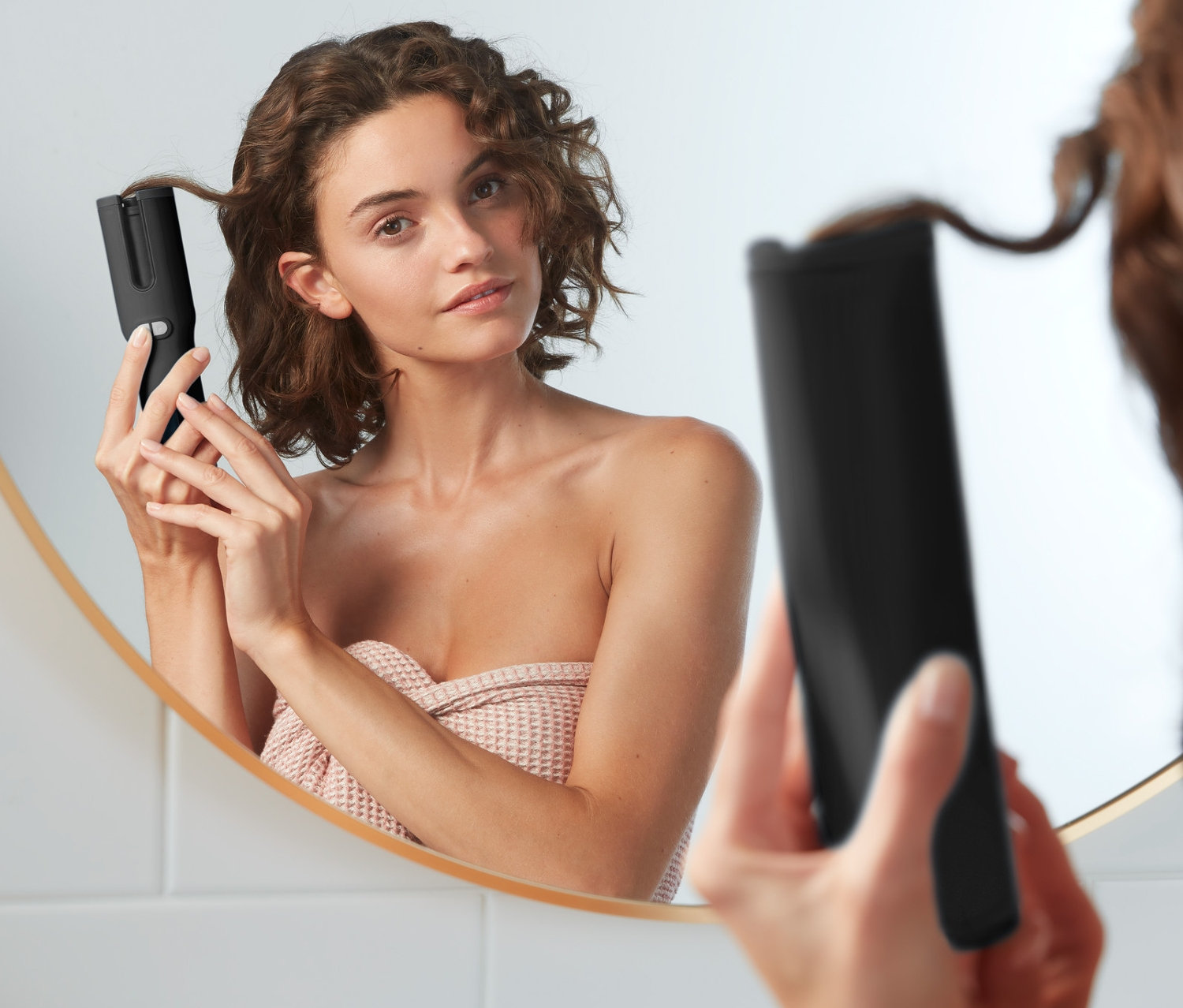 Kobieta kręci włosy lokówką automatyczną przed lustrem.