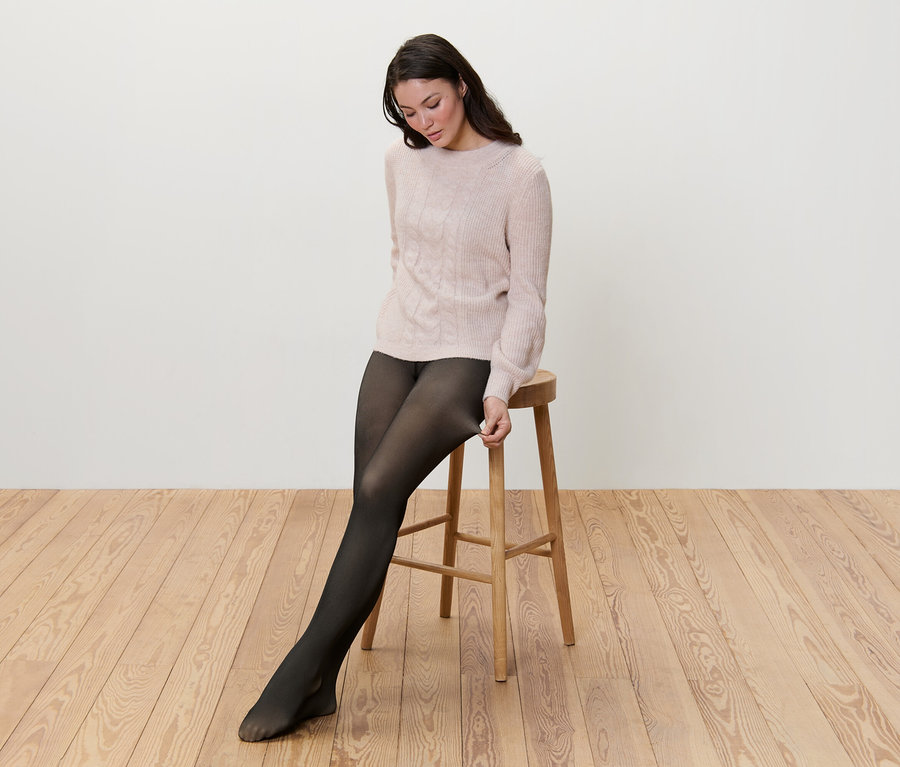 Kobieta siedzi na stołku i naciąga ocieplane rajstopy z efektem przezroczystości.