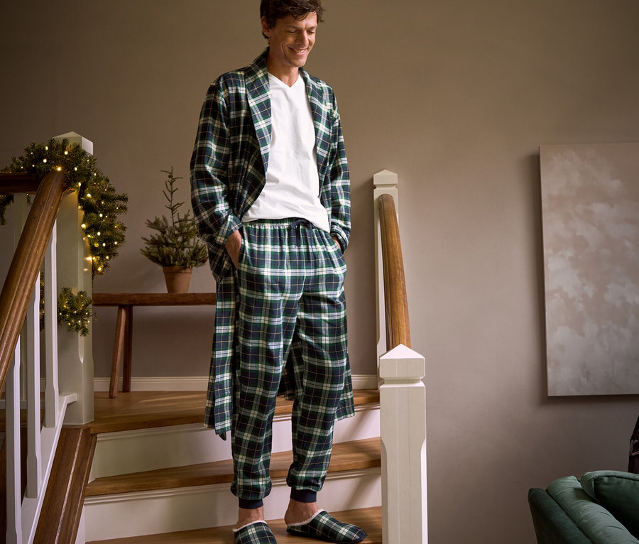 Mężczyzna schodzi po schodach w flanelowym szlafroku w kratę, flanelowych spodniach rekreacyjnych, kapciach i podkoszulku z dekoltem w serek.