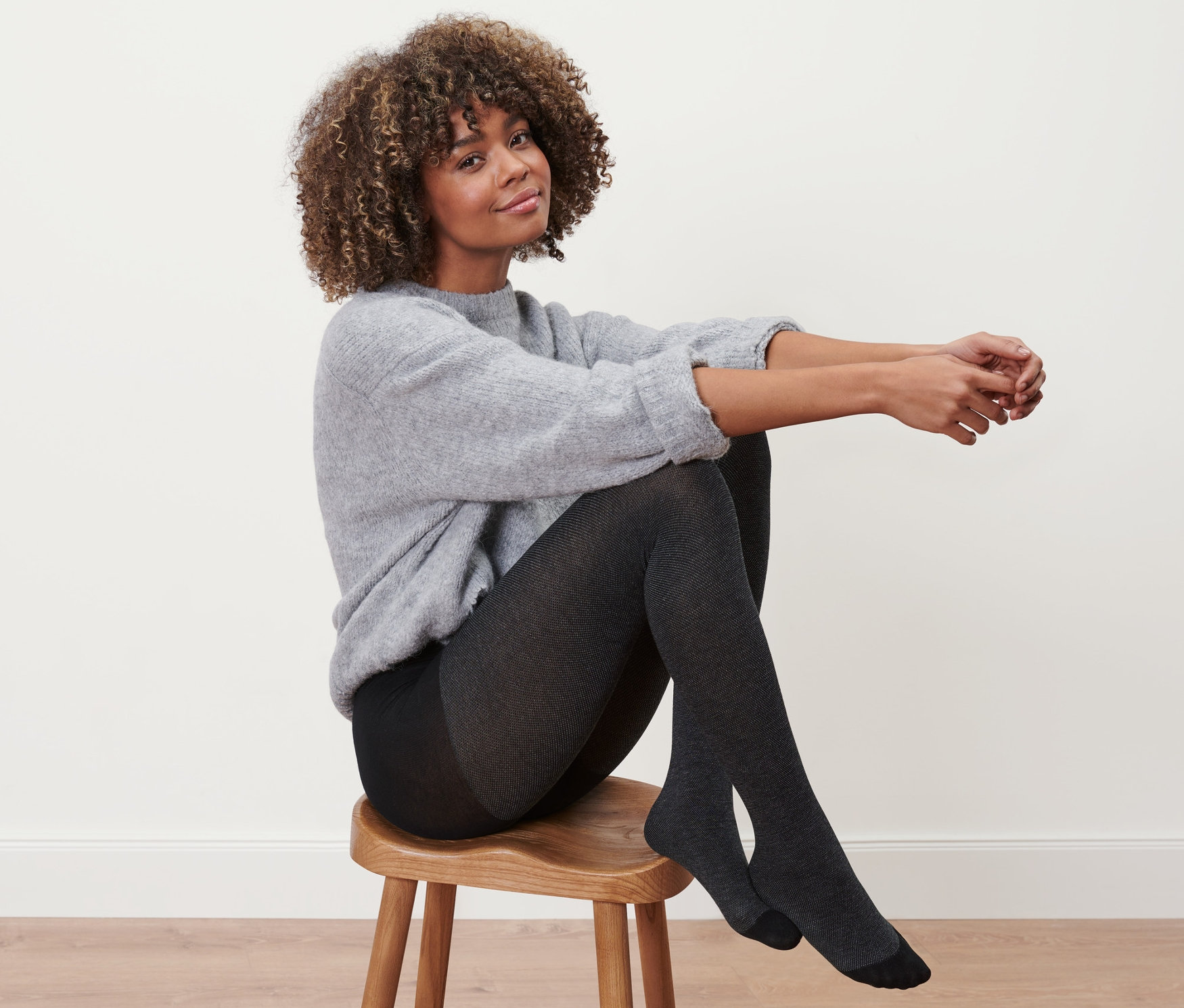 Kobieta siedzi na stołku i ma na sobie rajstopy ze strukturą.