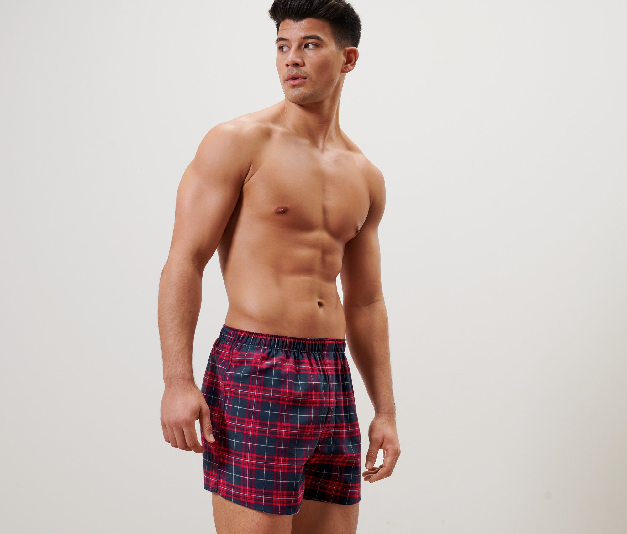 Mężczyzna pozuje w flanelowych szortach bokserkach w kratę.