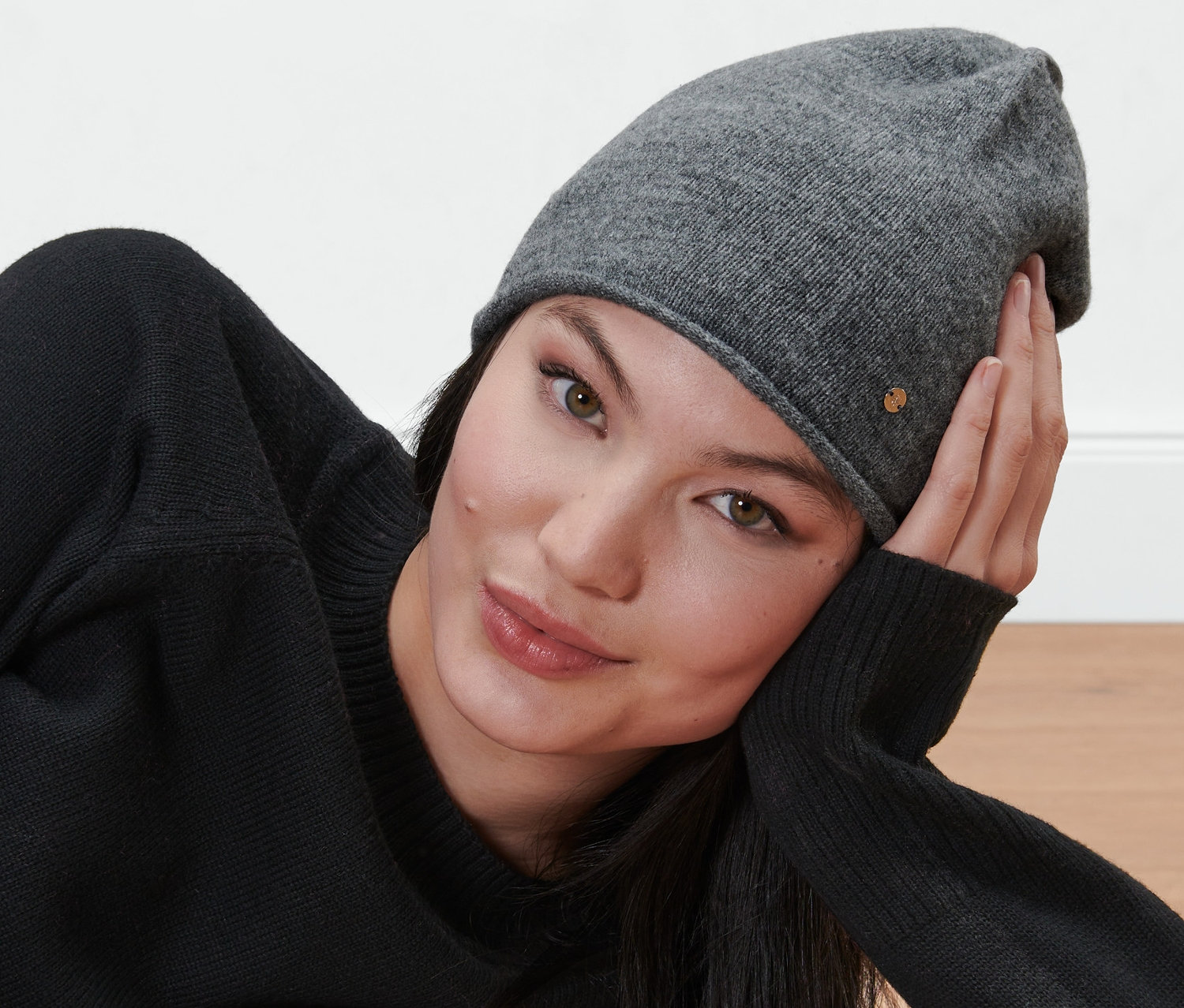 Kobieta leży, ma na sobie szarą czapkę z delikatnej dzianiny.