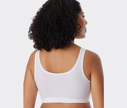 Widok z tyłu na kobietę z ciemnymi, kręconymi włosami, ubraną w biały biustonosz SCHIESSER z bawełny ekologicznej.