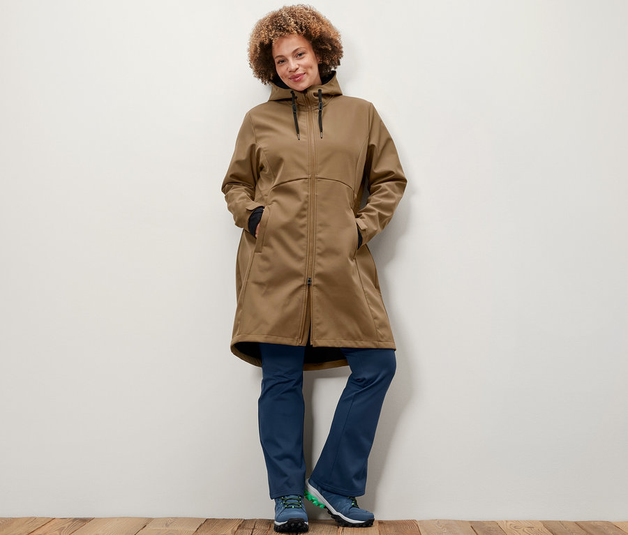 Kobieta pozuje w płaszczu softshellowym w kolorze nugatowym i termoaktywnych spodniach dzwonach.