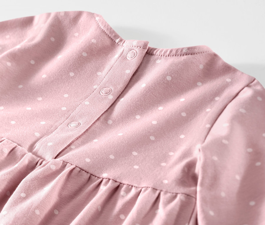 Zbliżenie na różową sukienkę dżersejową dla niemowląt w białe kropki, zapinaną na guziki.