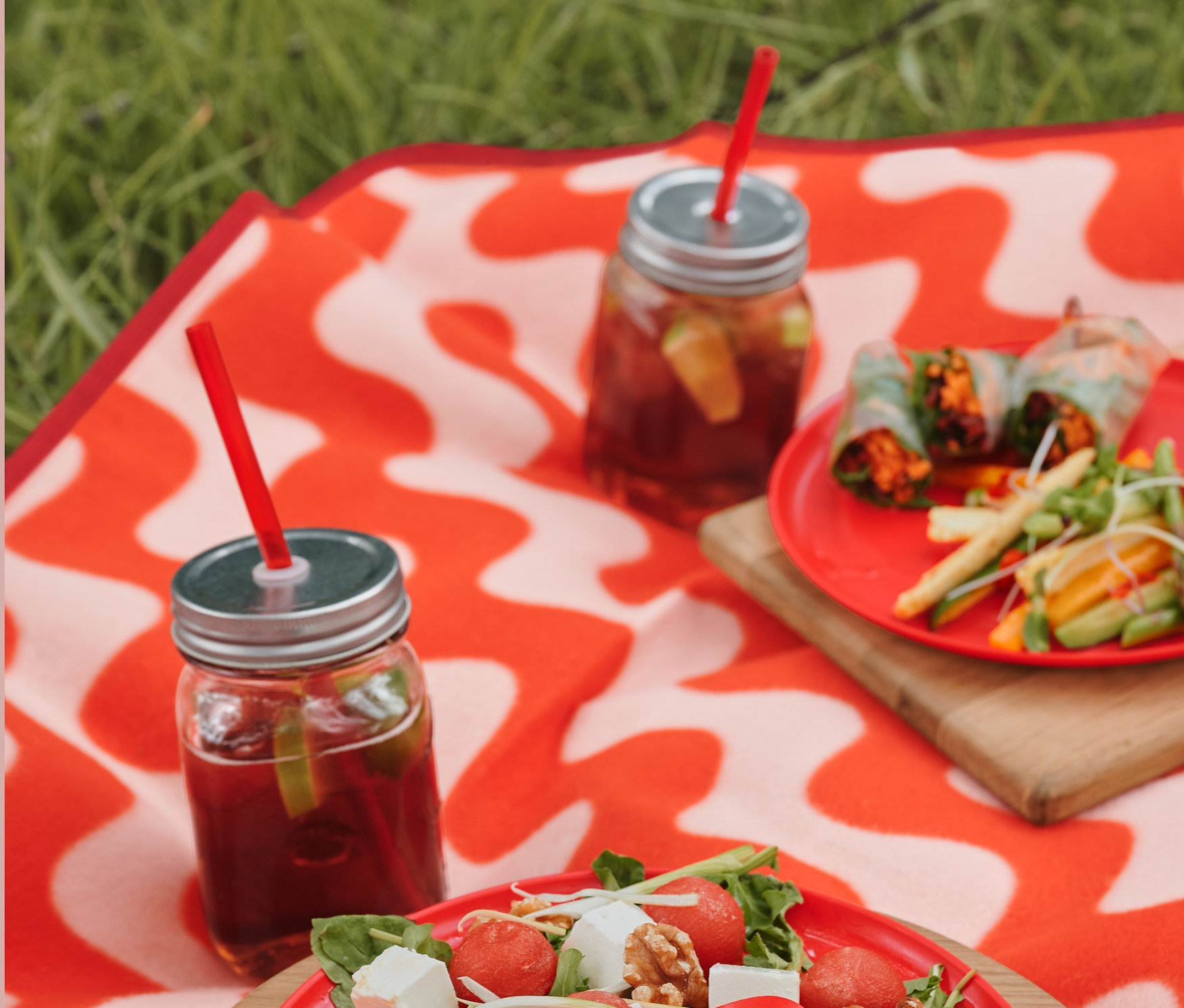 Na kocu piknikowym XL leżą talerze piknikowe z sałatką, sztućce piknikowe oraz szklanki z napojami i plastikowe słomki, 4 sztuki.