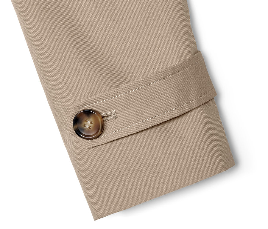 Detal beżowego trenczu z brązowym guzikiem.