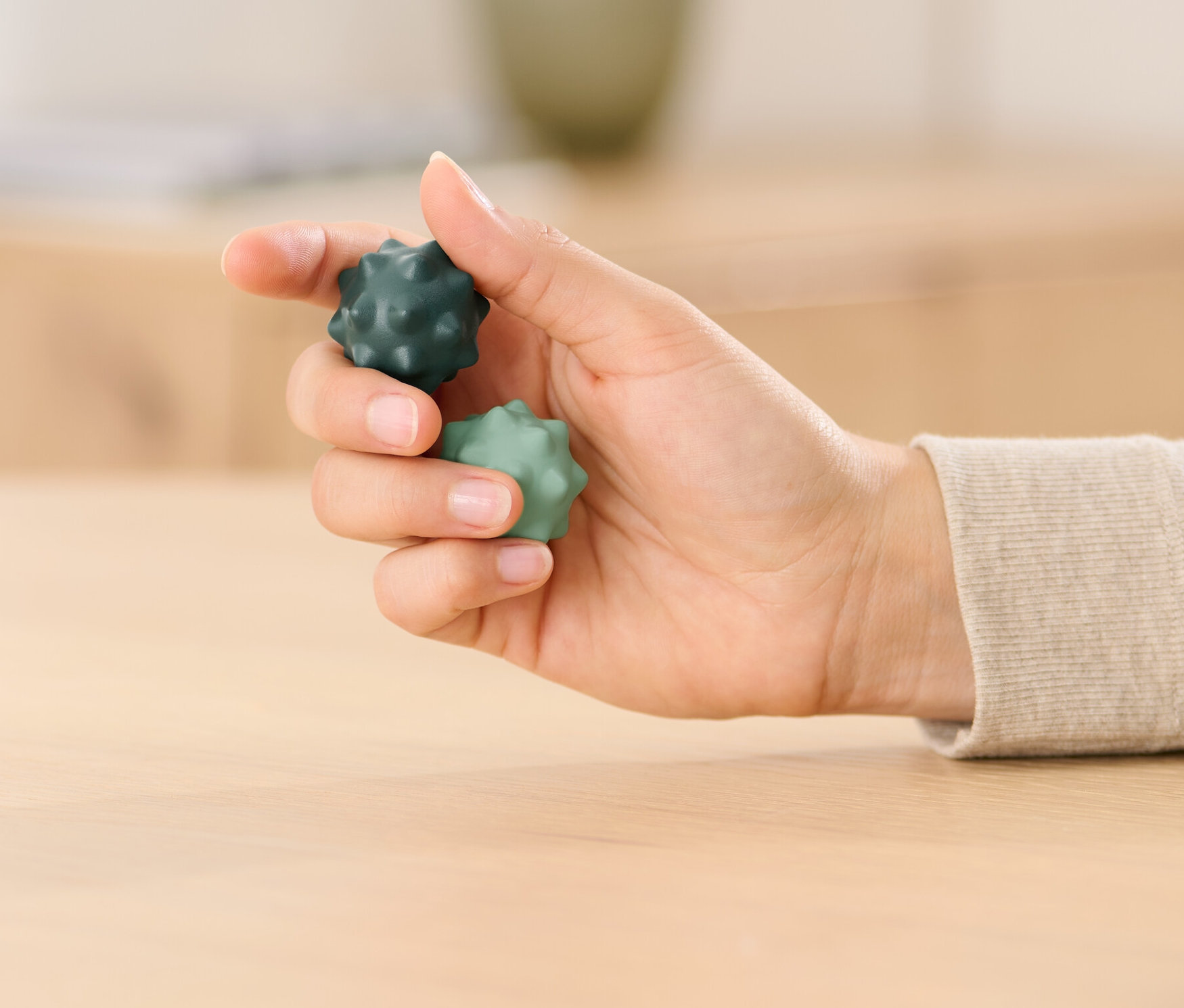 Kobieta trzyma w dłoni dwie kulki do ćwiczeń palców Qi Gong, jedną ciemnozieloną i jedną jasnozieloną.