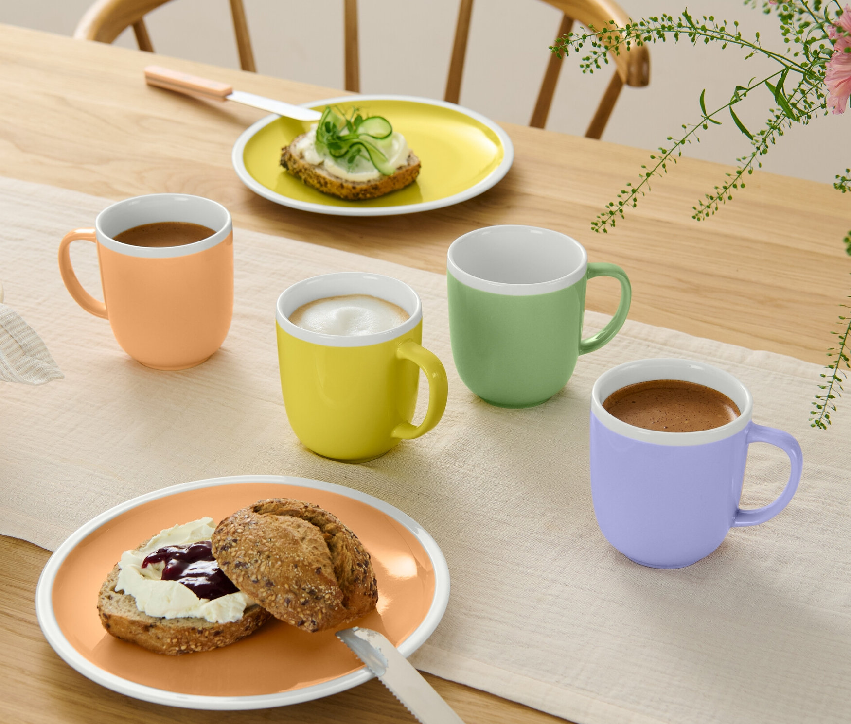 Cztery kubki w różnych kolorach stoją na stole obok talerzy z jedzeniem.