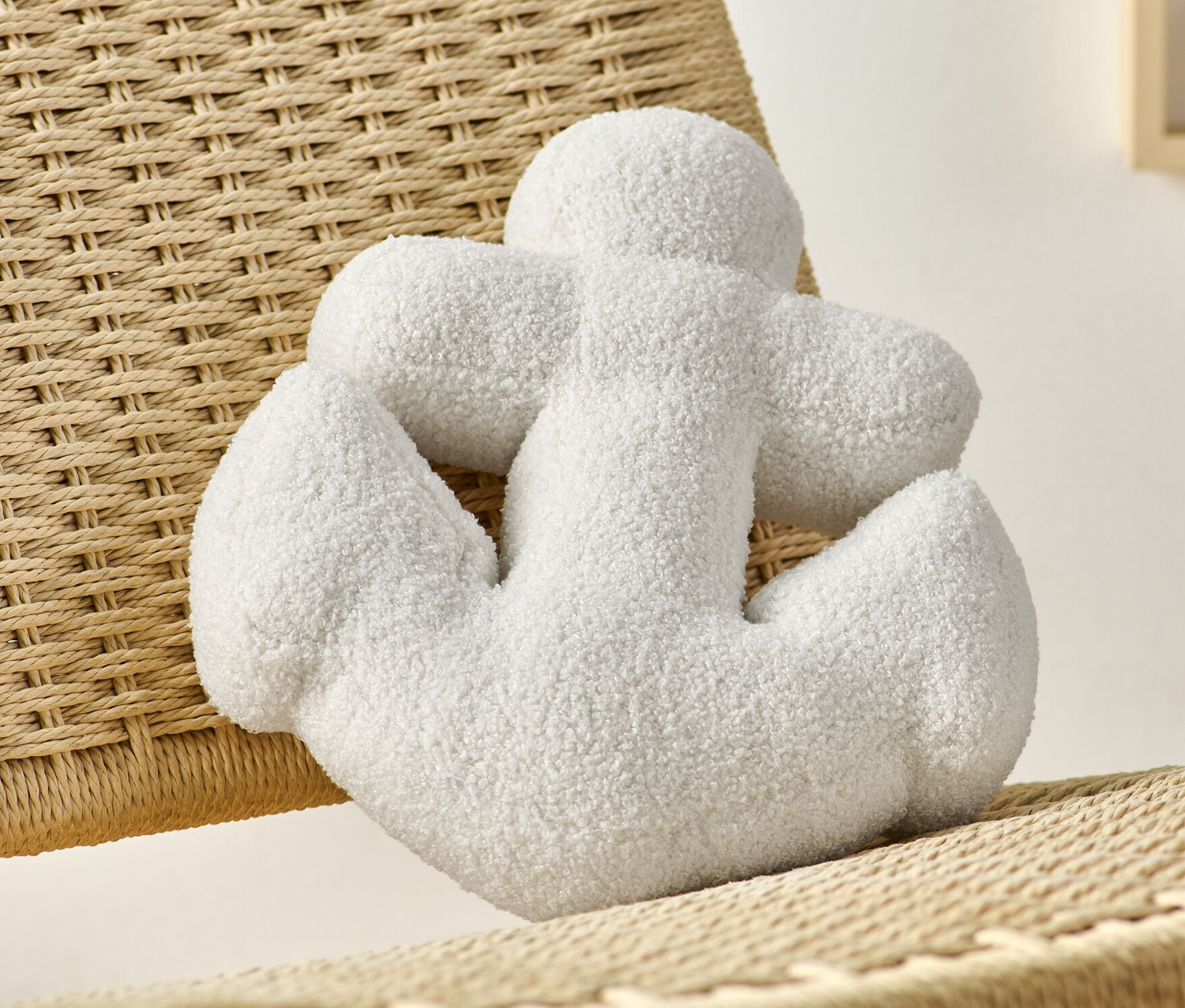 Biała poduszka dekoracyjna „Kotwica” leży na wiklinowym krześle.