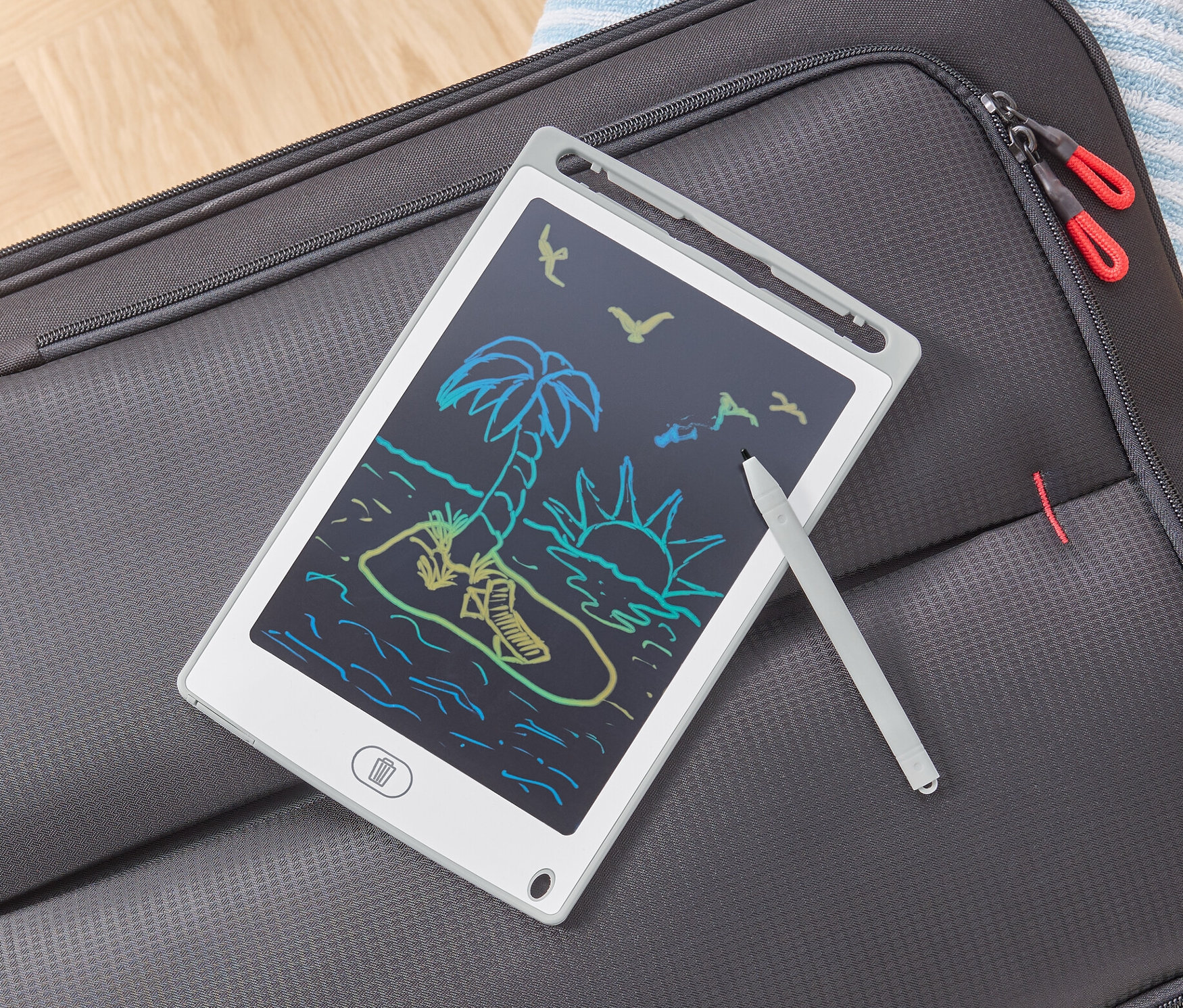 Tablet LCD do pisania z rysunkiem plaży leży na szarej walizce.