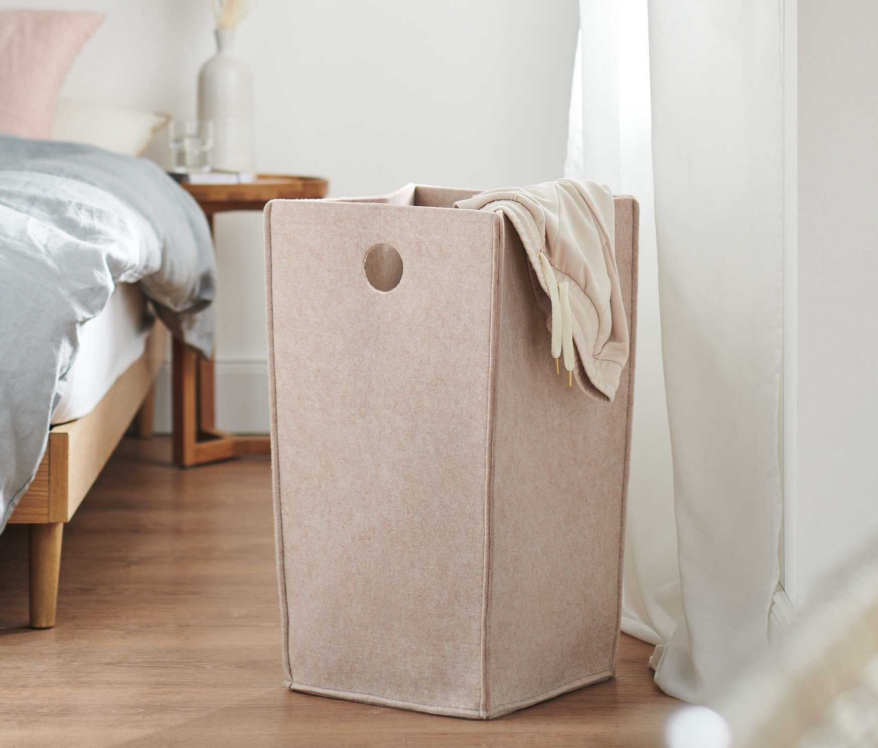 Kosz filcowy stoi na drewnianej podłodze obok łóżka.