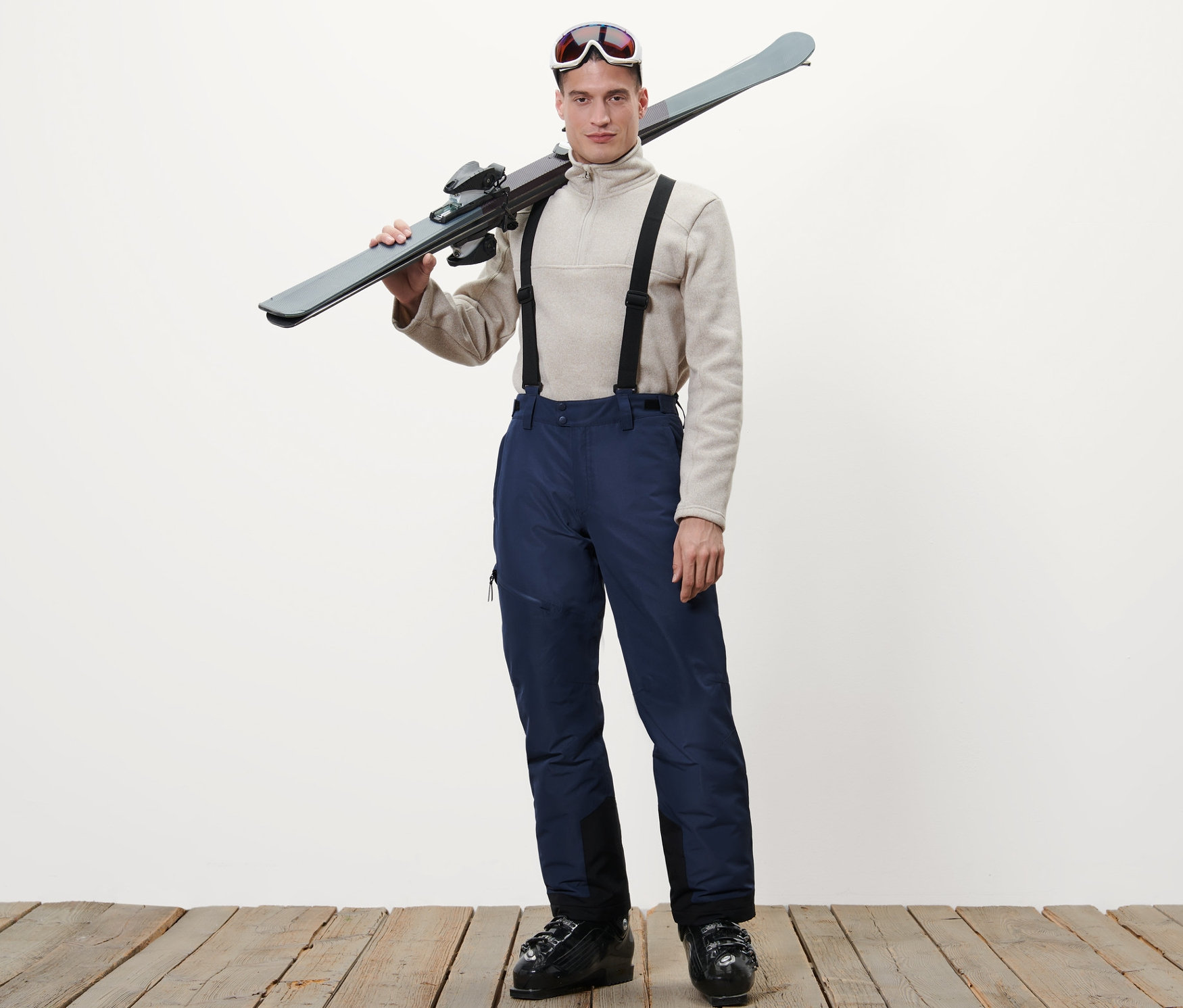 Mężczyzna z nartami na ramieniu, ubrany w niebieskie spodnie narciarskie.