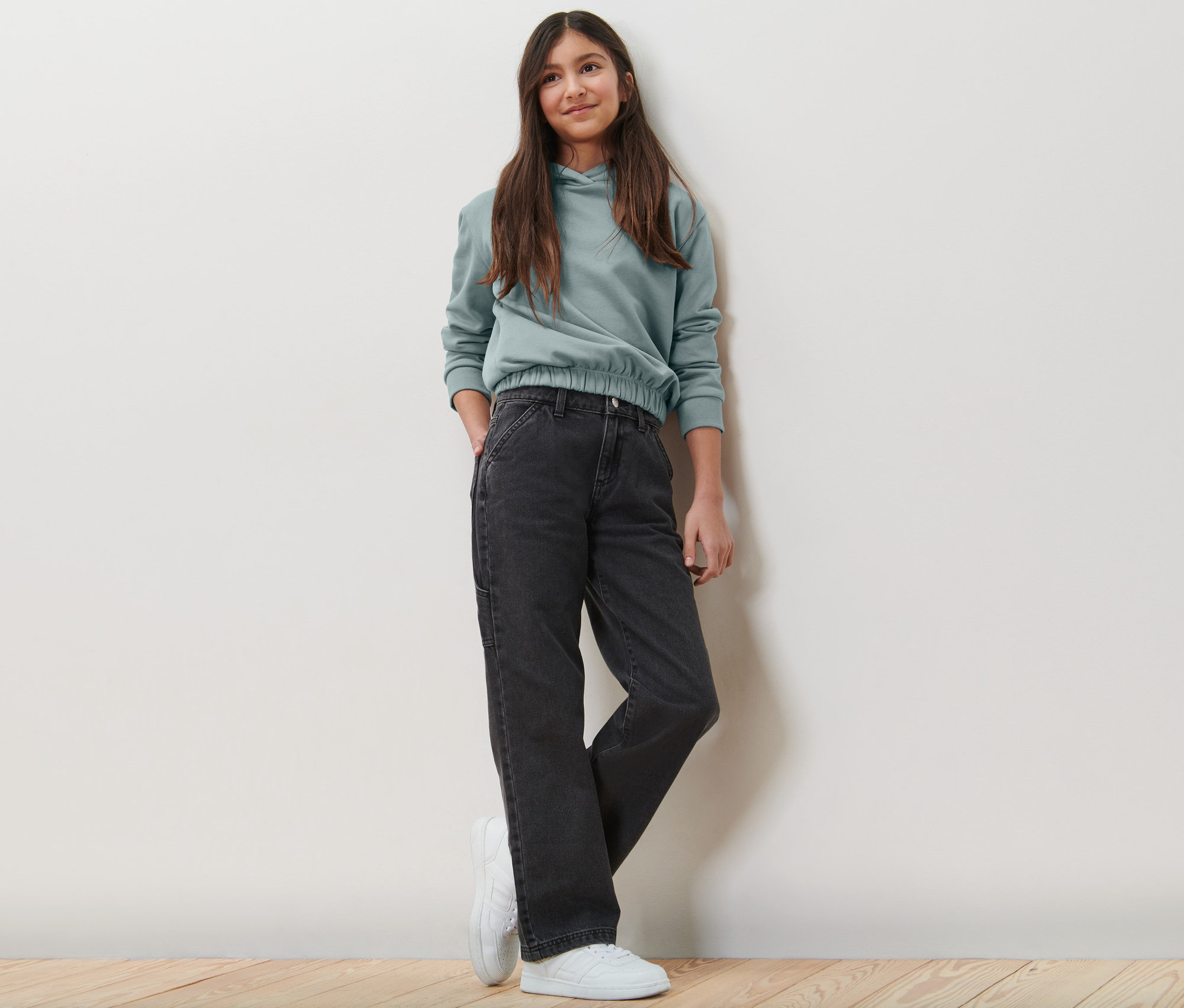 Dziewczyna pozuje w dziecięcych spodniach bojówkach i bluzie z kapturem.