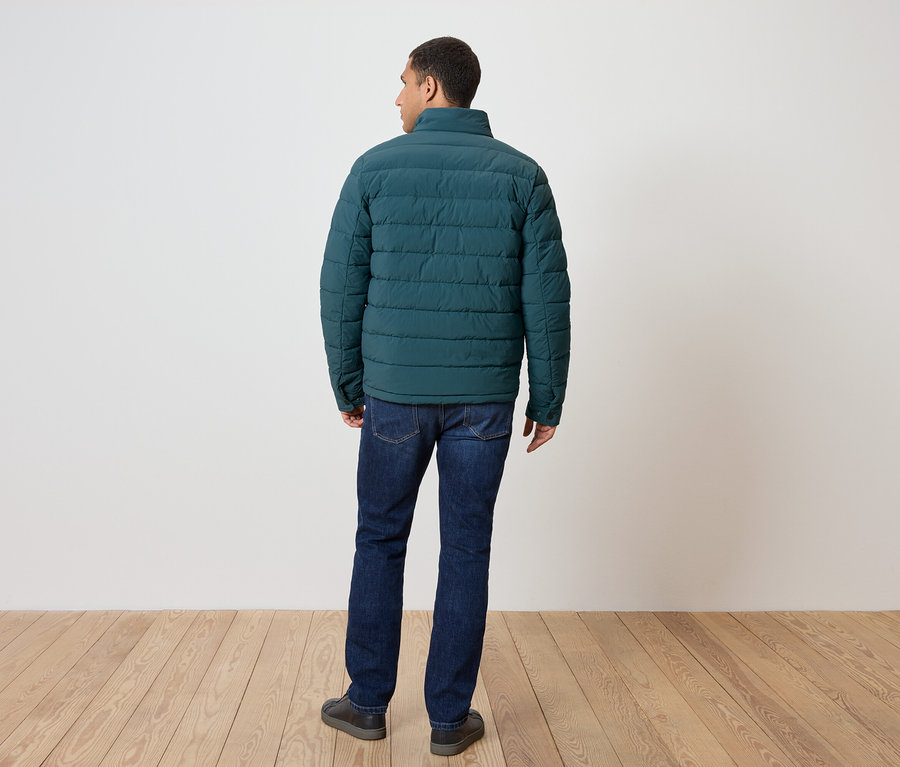 Mężczyzna tyłem do kamery ma na sobie zieloną kurtkę puchową, dżinsy i buty.