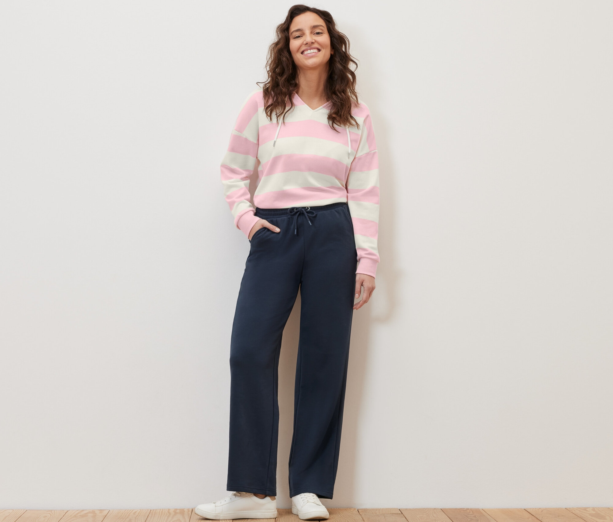 Kobieta stoi i pozuje w granatowych spodniach dresowych i bluzie w paski.