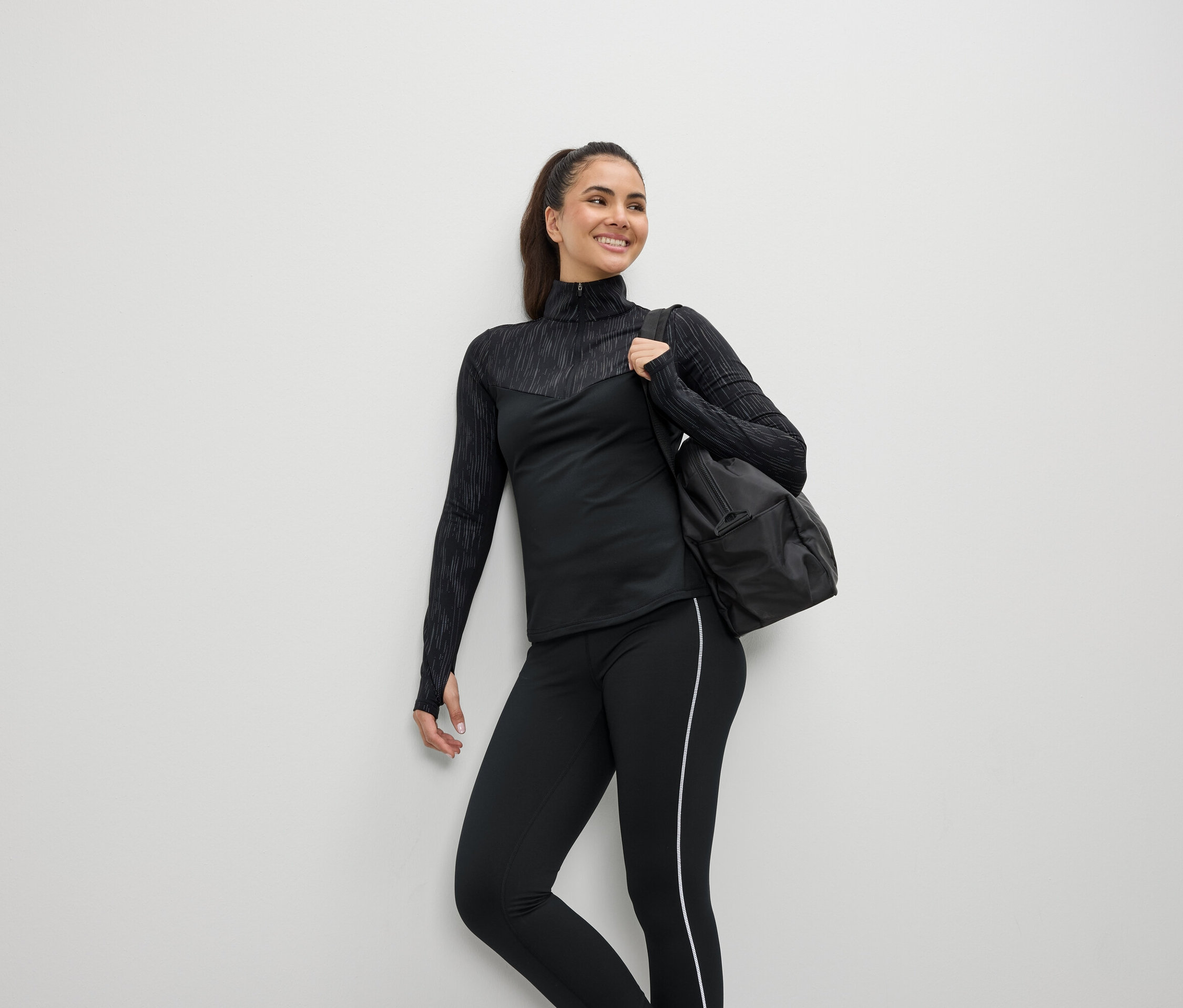 Uśmiechnięta kobieta w czarnym stroju sportowym z torbą na ramieniu.