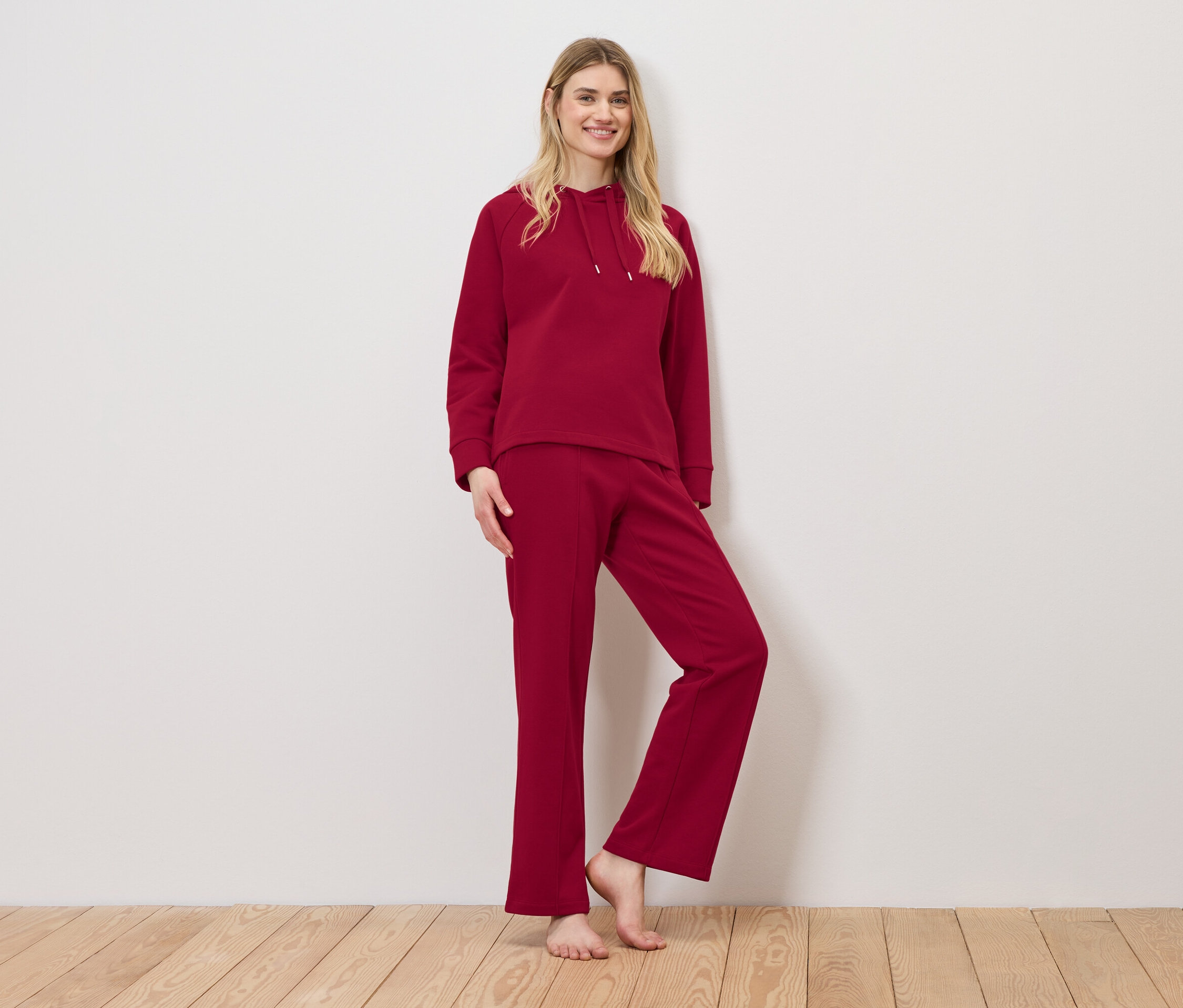 Kobieta pozuje w czerwonym dresie składającym się z bluzy z kapturem i spodni dresowych.