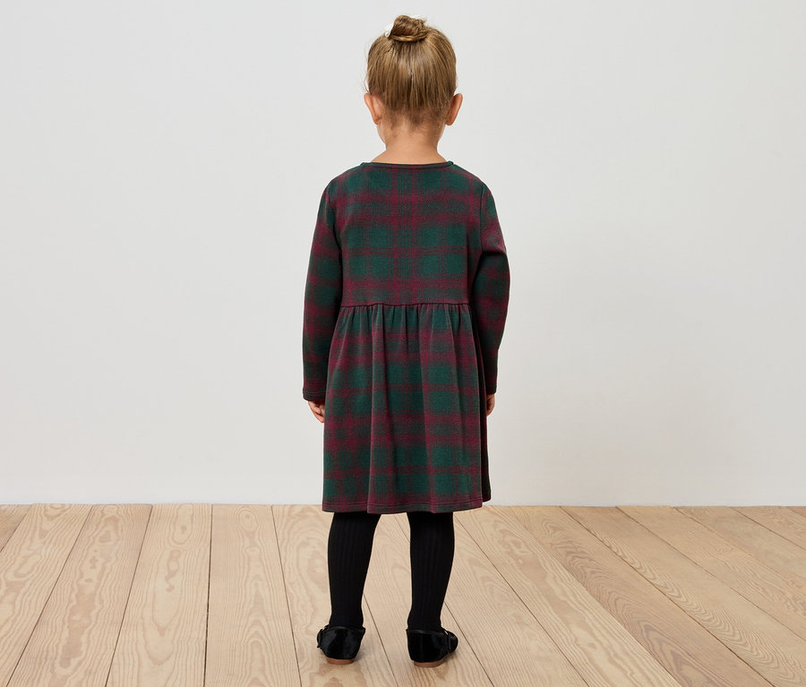 Dziewczynka w sukience w kratę stoi tyłem do kamery.