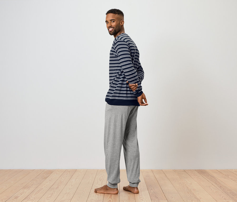 Mężczyzna spogląda przez ramię i uśmiecha się. Ma na sobie bluzkę w paski i szare spodnie dresowe.
