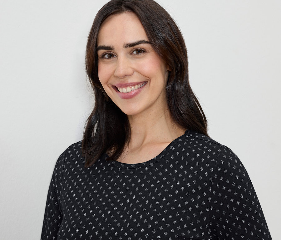 Uśmiechnięta kobieta z brązowymi włosami w czarno-białej sukience.