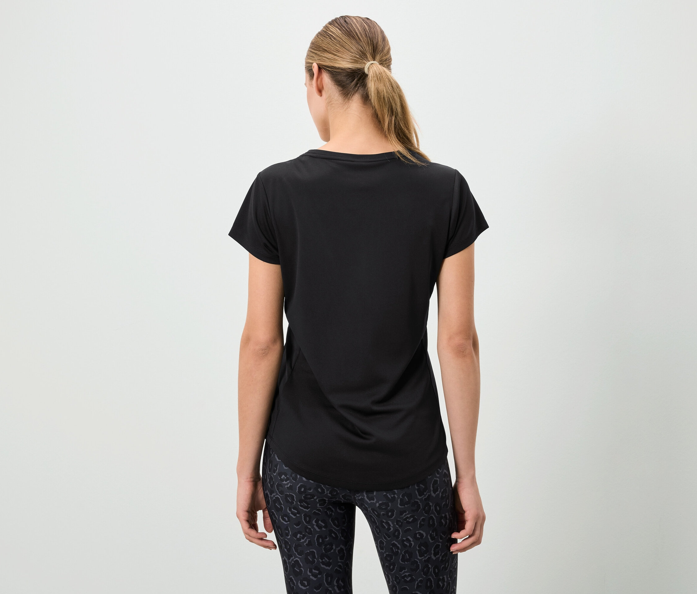 Kobieta tyłem do kamery ma na sobie czarną koszulkę i wzorzyste legginsy.