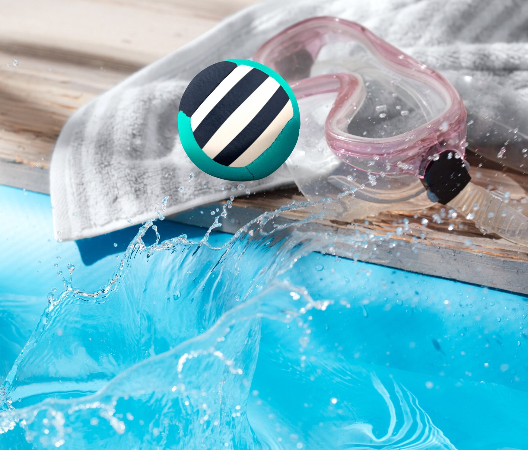 Skacząca piłka do zabawy w wodzie ląduje w basenie obok ręcznika i okularów.