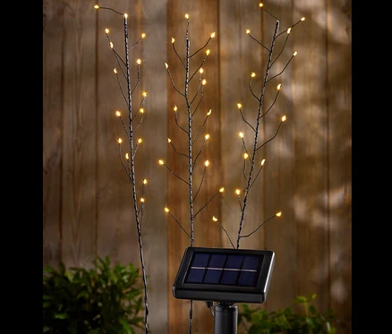 Trzy lampy solarne do wbicia w ziemię z diodami LED na tle drewnianej ściany.