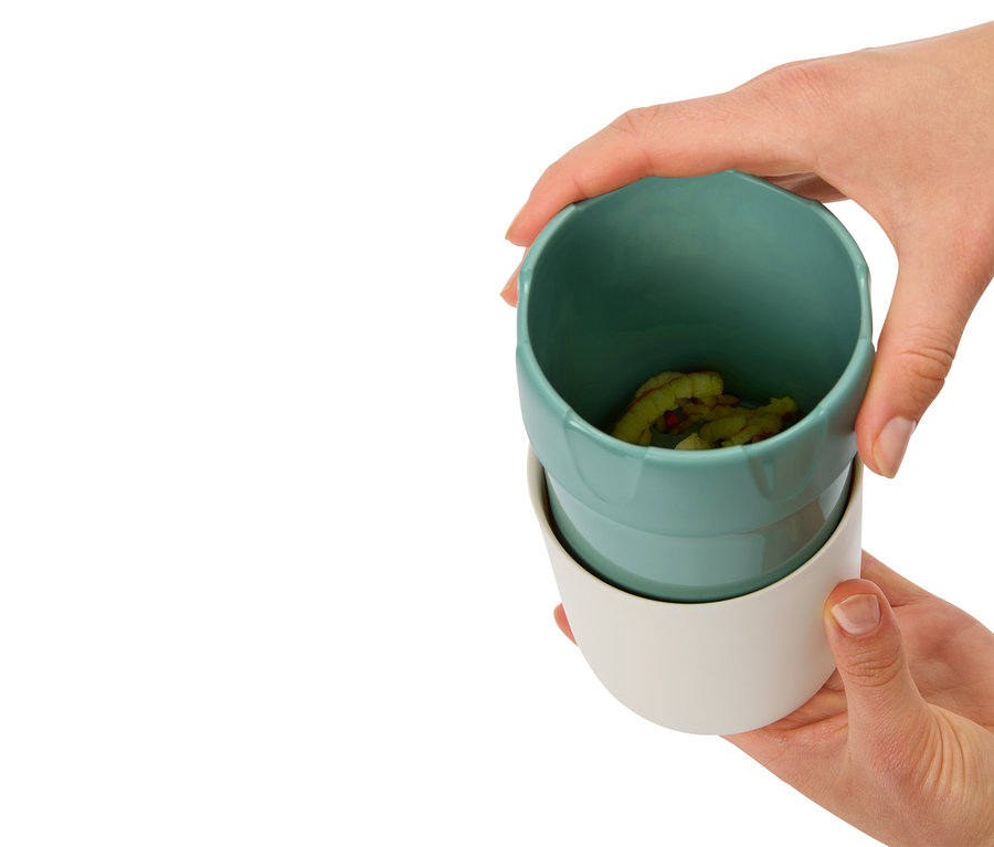 Dłonie trzymają dwa kubki, górny jest turkusowy z zawartością, dolny biały.