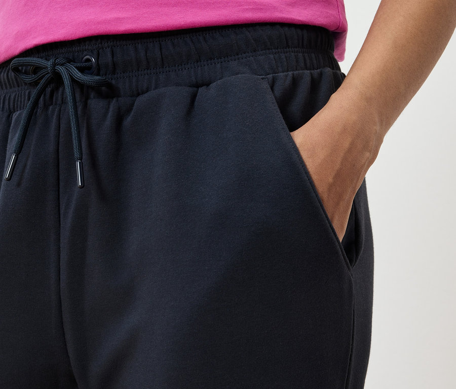 Zbliżenie na granatowe spodnie dresowe z ręką w kieszeni i różową koszulką.