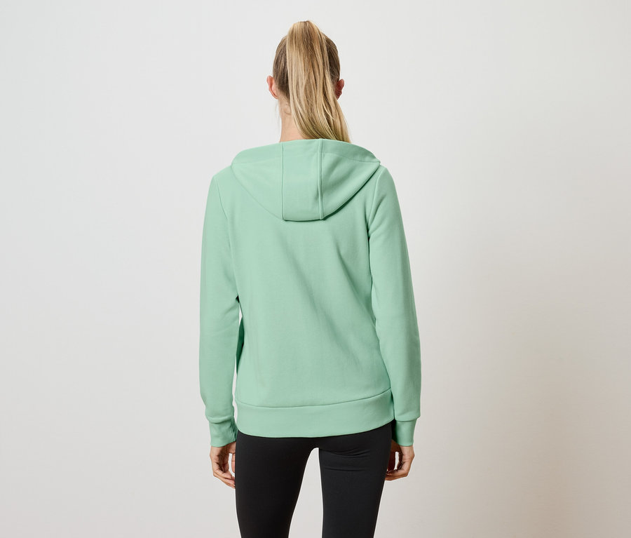 Widok z tyłu kobiety z blond włosami związanymi w kucyk, ubranej w jasnozieloną bluzę z kapturem i czarne legginsy.