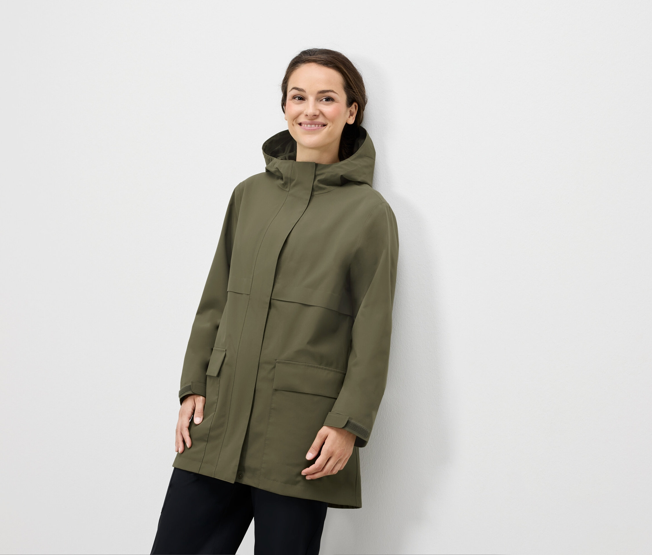 Kobieta pozuje w oliwkowozielonej kurtce z kapturem i czarnych spodniach.