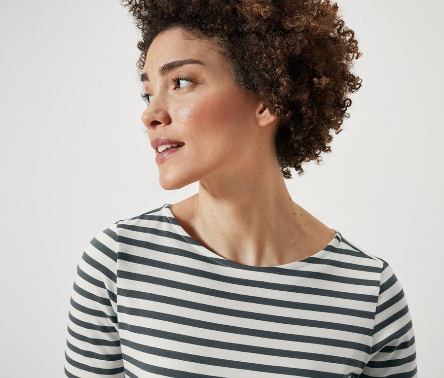 Portret kobiety z krótkimi kręconymi włosami. Ma na sobie koszulkę w zielone paski z krótkim rękawem.