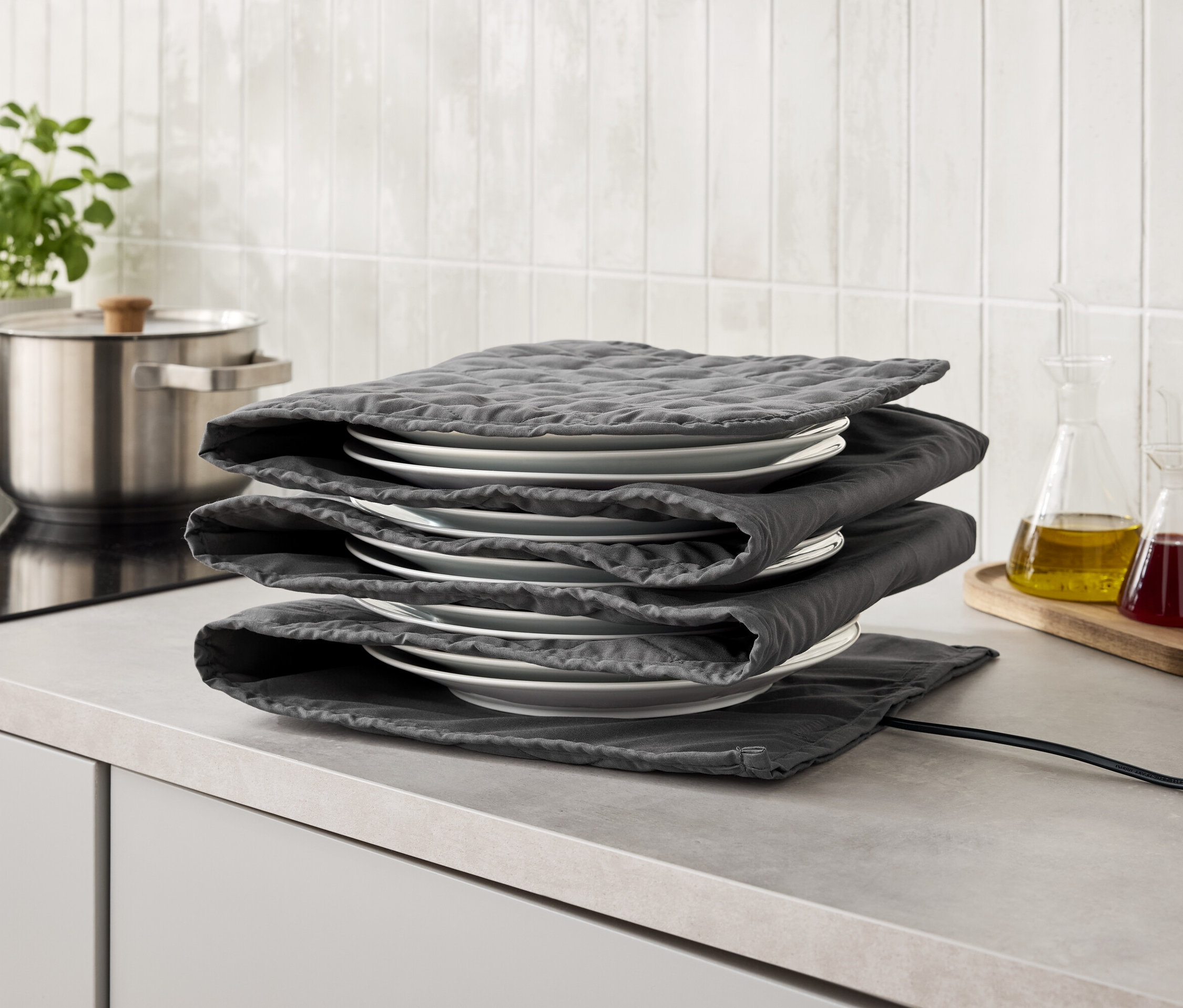 Stos białych talerzy owiniętych szarymi podkładkami z materiału na szarym blacie kuchennym.