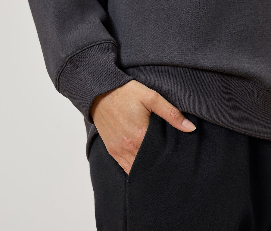 Zbliżenie na kobietę z ręką w kieszeni czarnych spodni dresowych, w szarej bluzie.