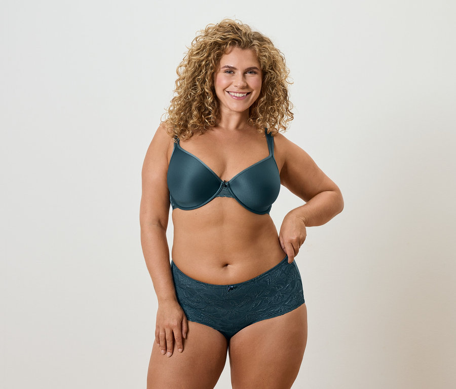 Kobieta z kręconymi blond włosami w petroliowym biustonoszu i pasującej do niego bieliźnie.