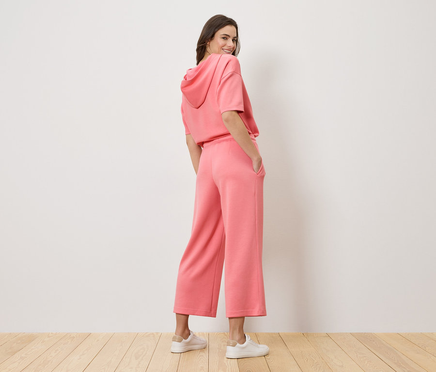 Kobieta spoglądająca przez ramię ma na sobie różową bluzę z kapturem i kuloty.