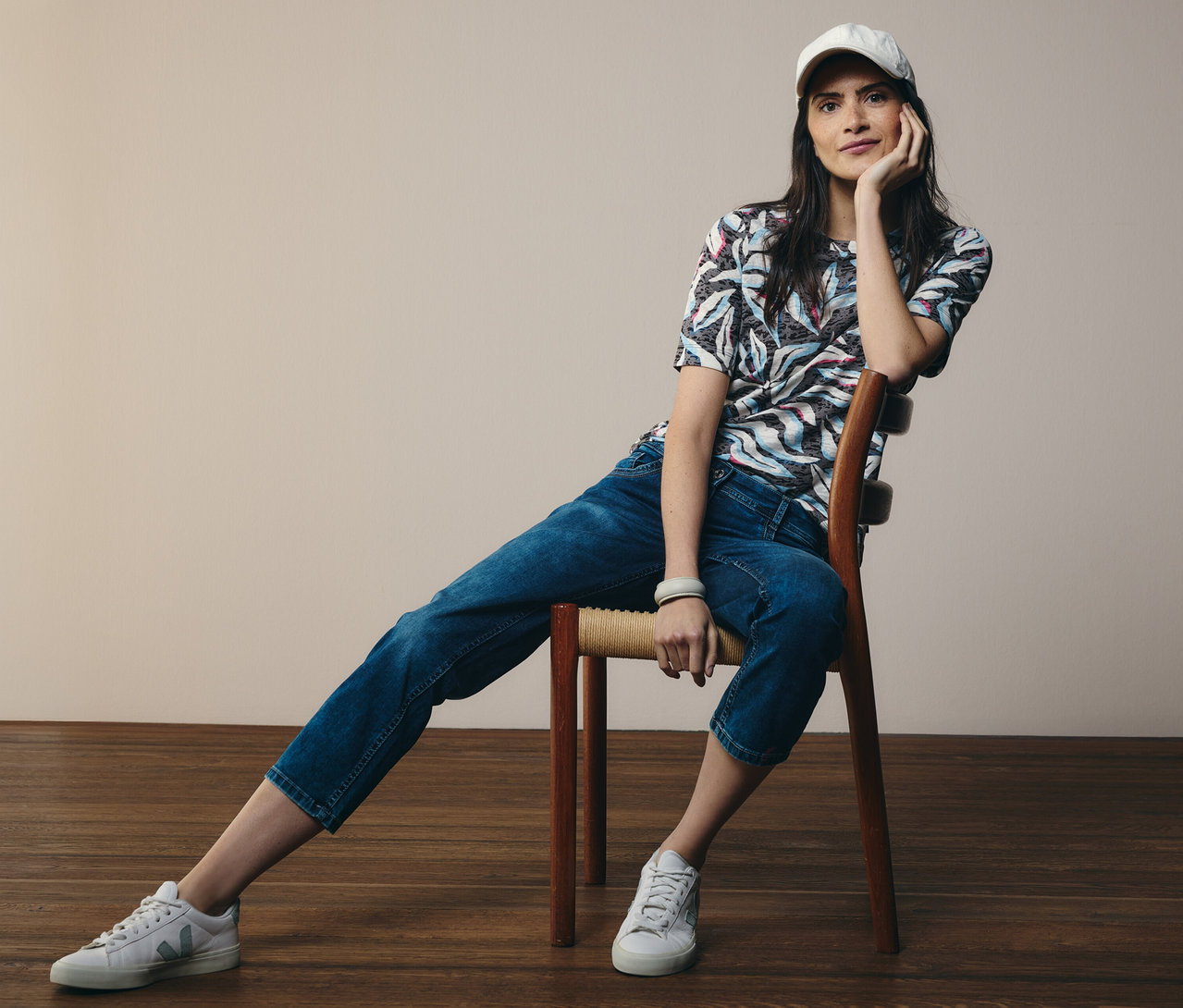 Kobieta siedzi na krześle, ma na sobie niebieską koszulkę z krótkim rękawem CECIL i dżinsy „Scarlett” CECIL.