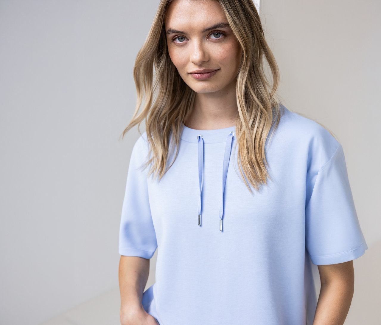 Kobieta ma na sobie błękitną koszulkę Street One ze sznurkami przy dekolcie.