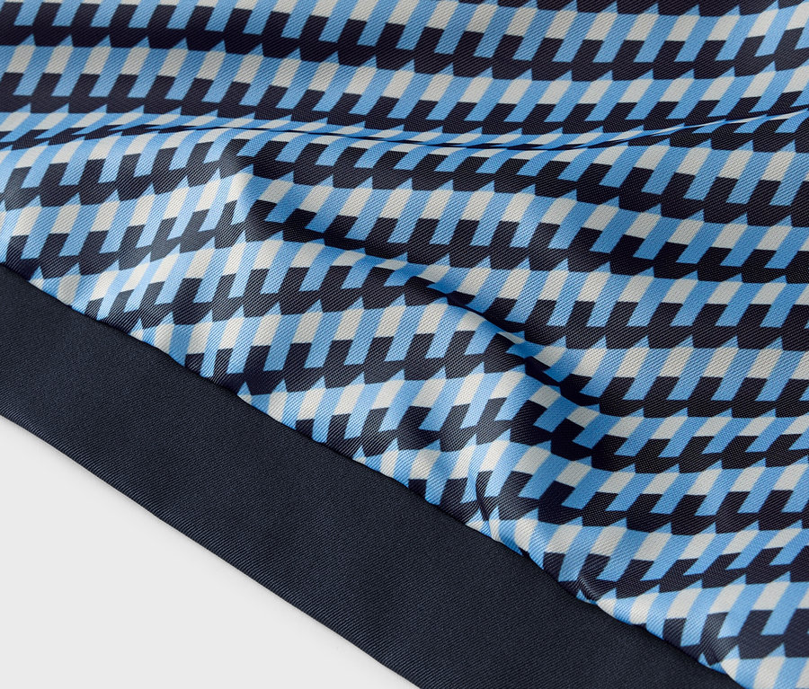 Zbliżenie tkaniny z niebieskim, jasnoniebieskim i białym geometrycznym wzorem oraz granatowym brzegiem.