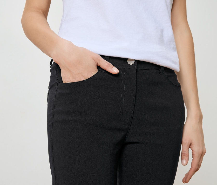 Kobieta z ręką w kieszeni czarnych spodni i białym T-shircie.