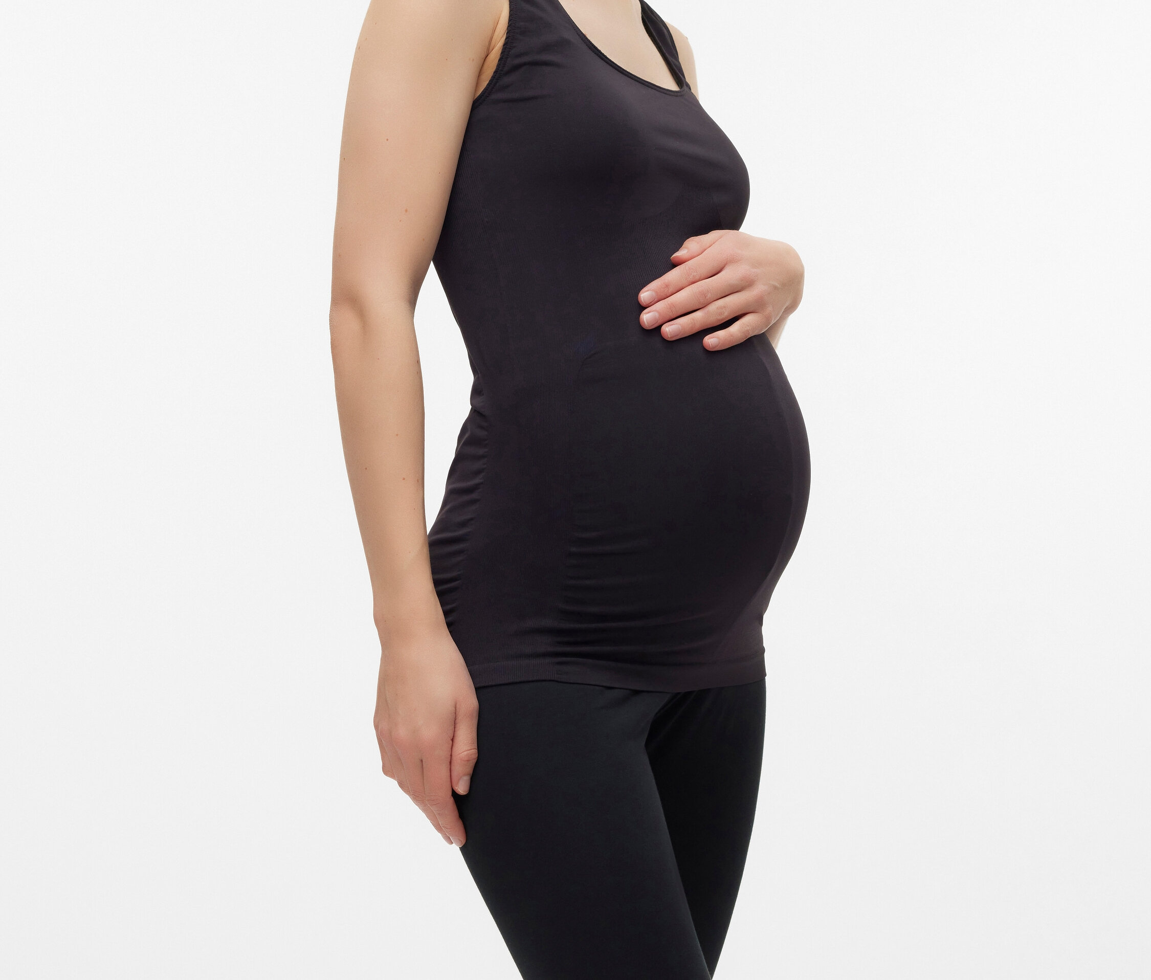 Kobieta w ciąży w czarnym tank topie i legginsach pozuje na białym tle.
