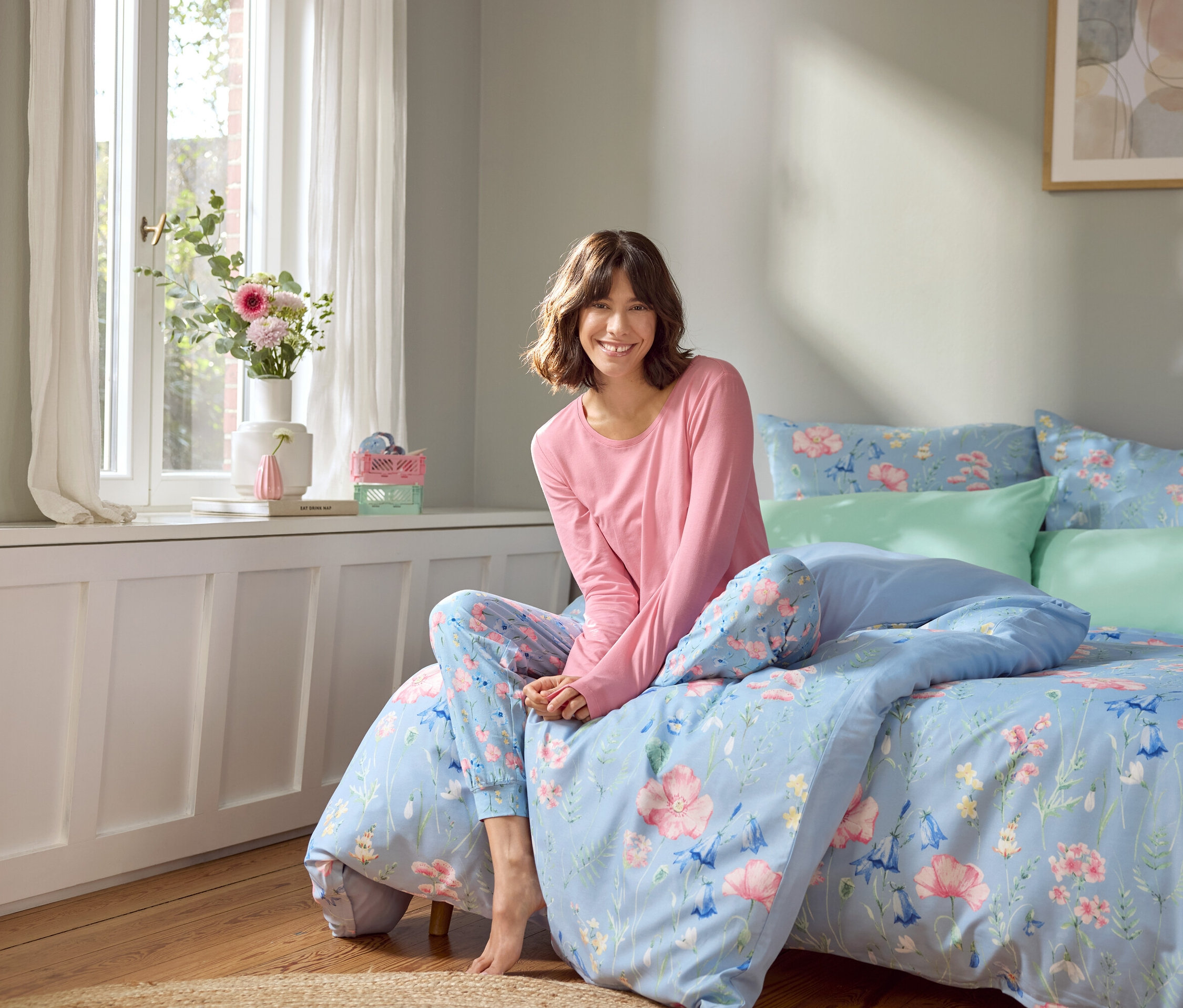 Kobieta siedzi na łóżku z jasnoniebieską pościelą w kwiaty.