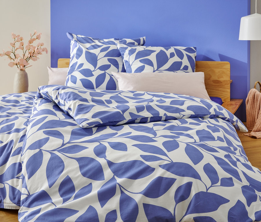 Łóżko z biało-niebieską pościelą w liście stoi na tle ściany pomalowanej na biało i niebiesko.