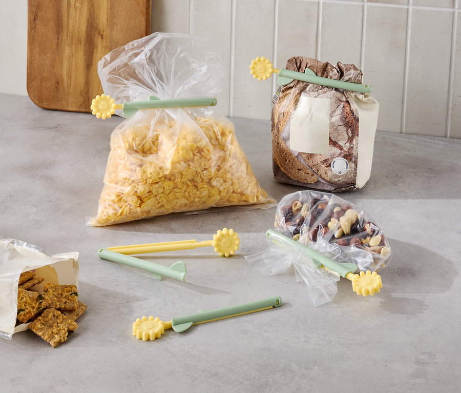 Różne produkty spożywcze zapakowane w torby z żółto-zielonymi klipsami na blacie kuchennym.