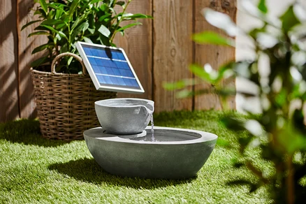 Szara solarna fontanna ogrodowa z dwiema misami na trawie.