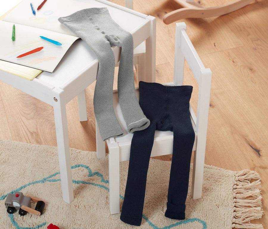 Na krześle leżą legginsy termoaktywne: szare melanż i granatowe. Na stole kredki i papier. W tle drewniany koń na biegunach.
