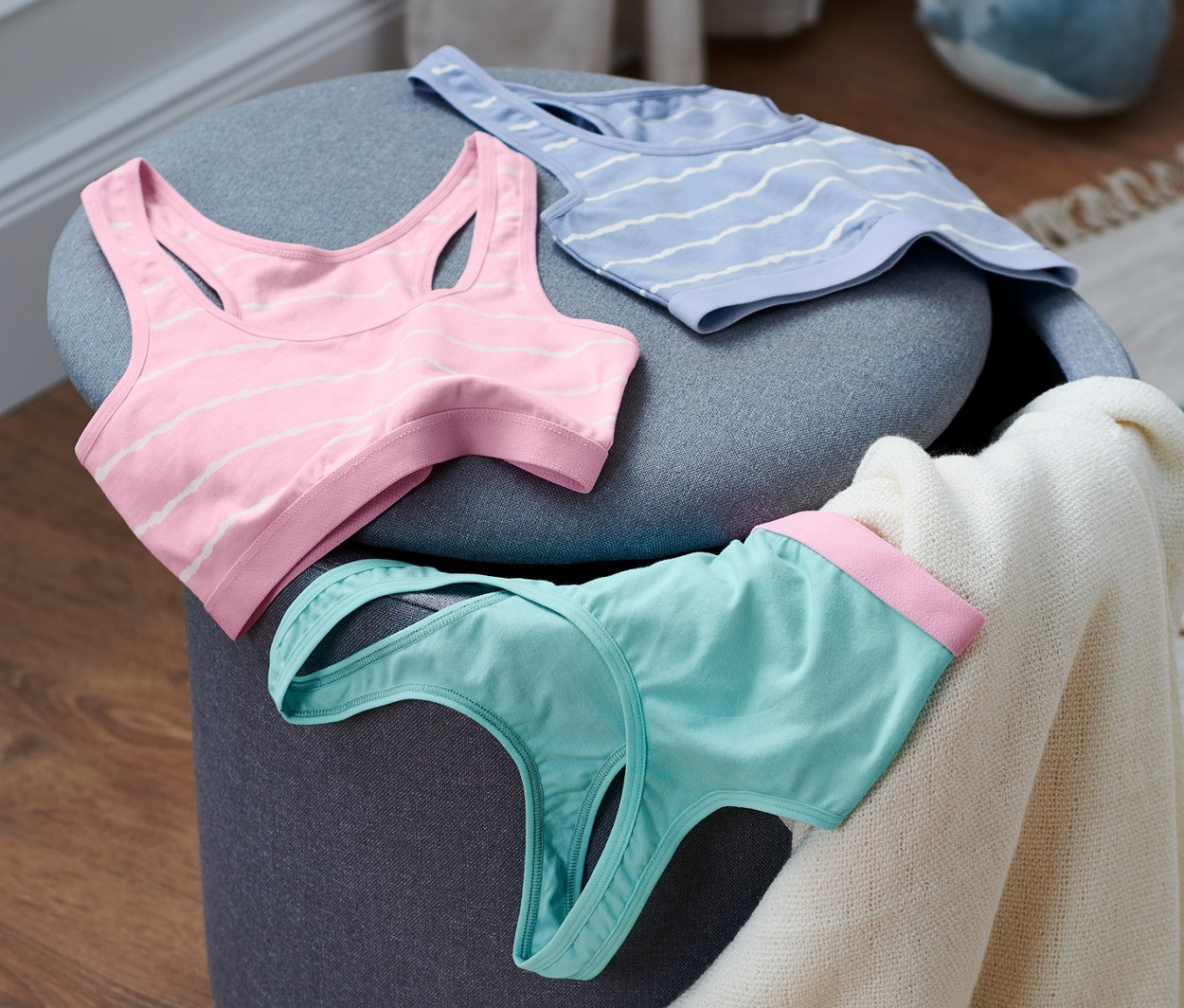 Na szarym stołku leżą trzy biustonosze gorsetowe z biobawełny.