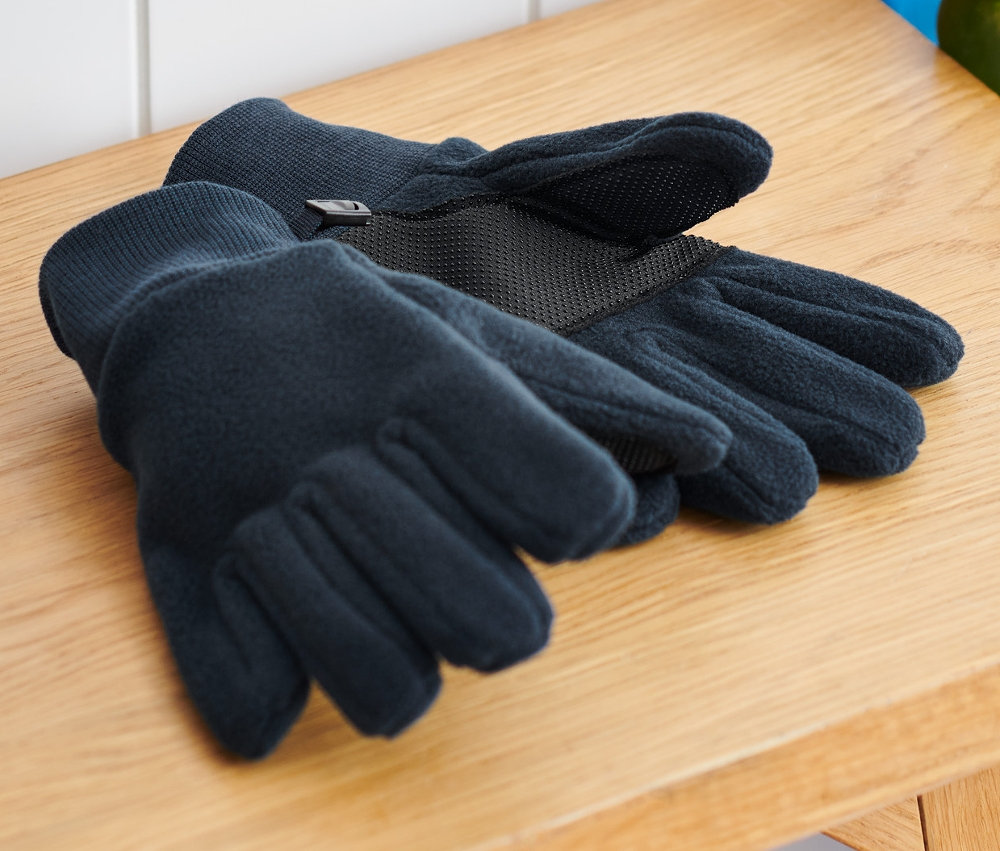 Dziecięce rękawiczki z polaru leżą na drewnianej ławce obok plecaka i deskorolki.